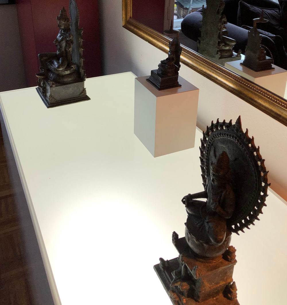 Three intricate black statues displayed on a bright table, reflecting in a nearby mirror.