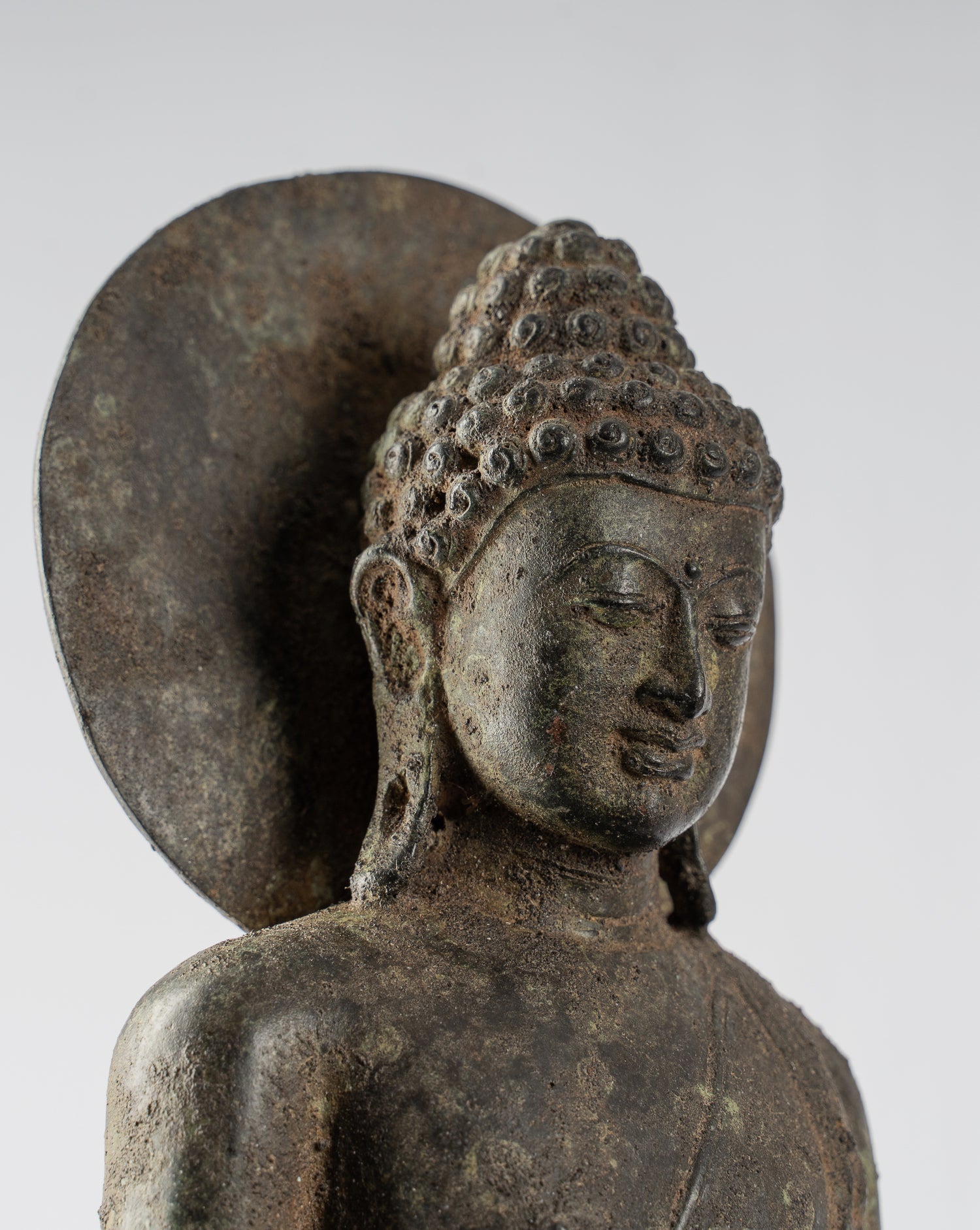 Bronze Buddha statue with detailed hair, serene expression, and circular halo background.